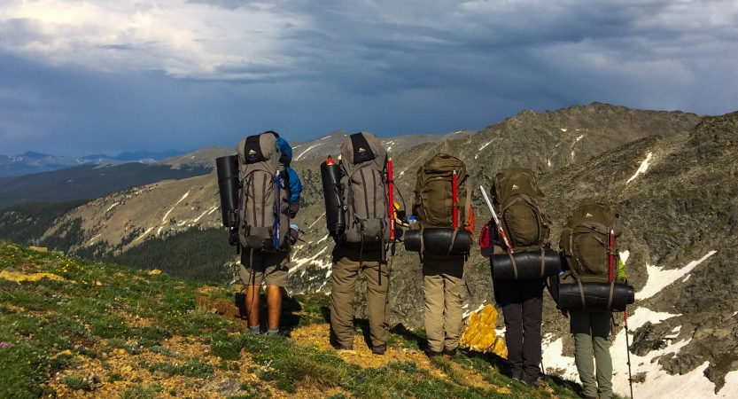 Five people with backpacks overlook a mountainous landscape